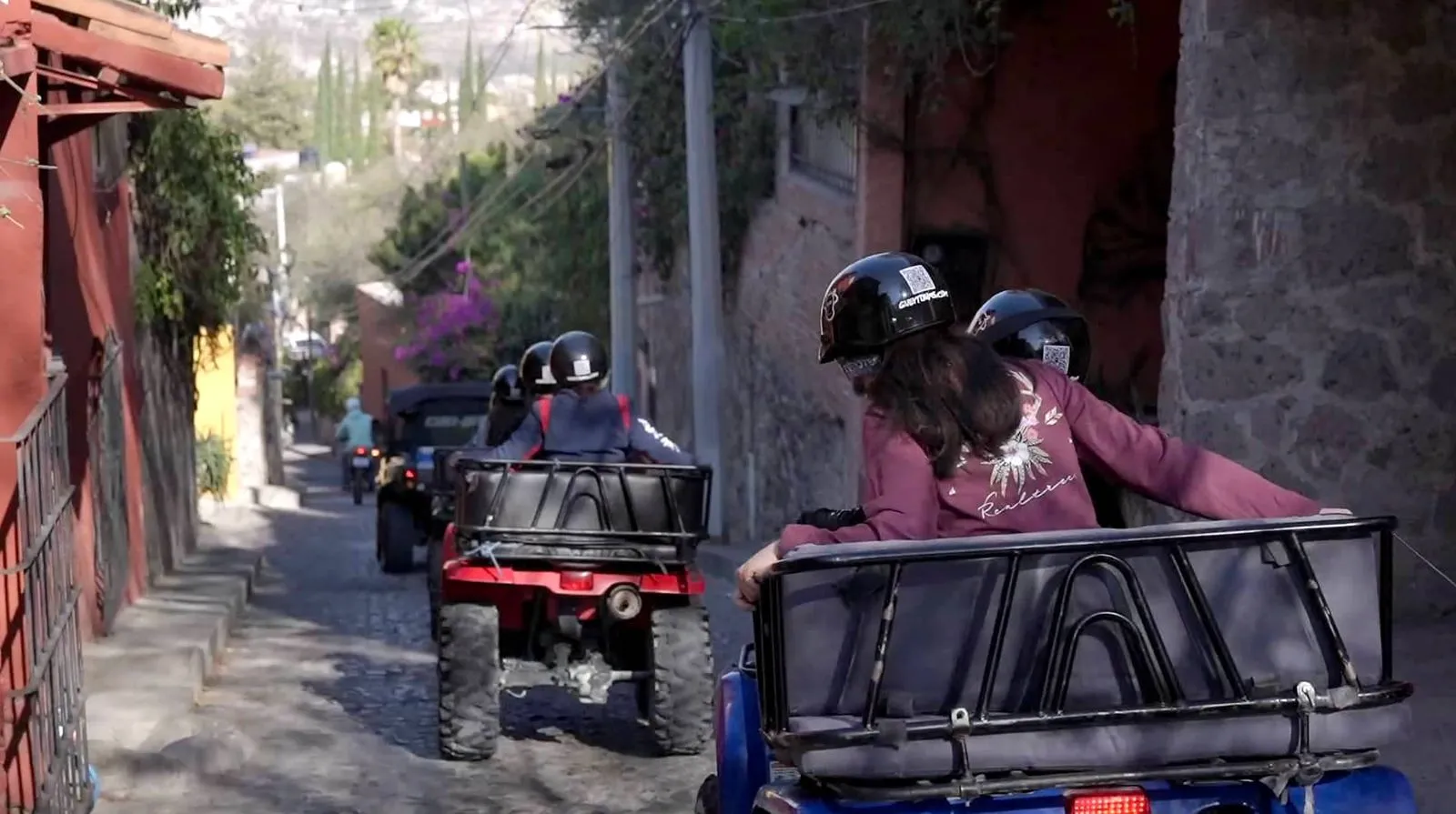Group riding all-terrain vehicles during guided outdoor UTV tours Group of people wearing safety helmets driving off-road vehicles down a narrow stone street during UTV tours.